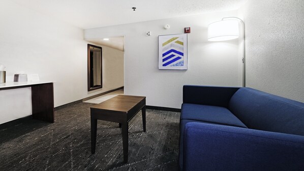 A hotel lobby with a reception desk, a blue sofa, a small table, and a framed artwork on the wall. - Holiday Inn Exp Walterboro by IHG (Walterboro)