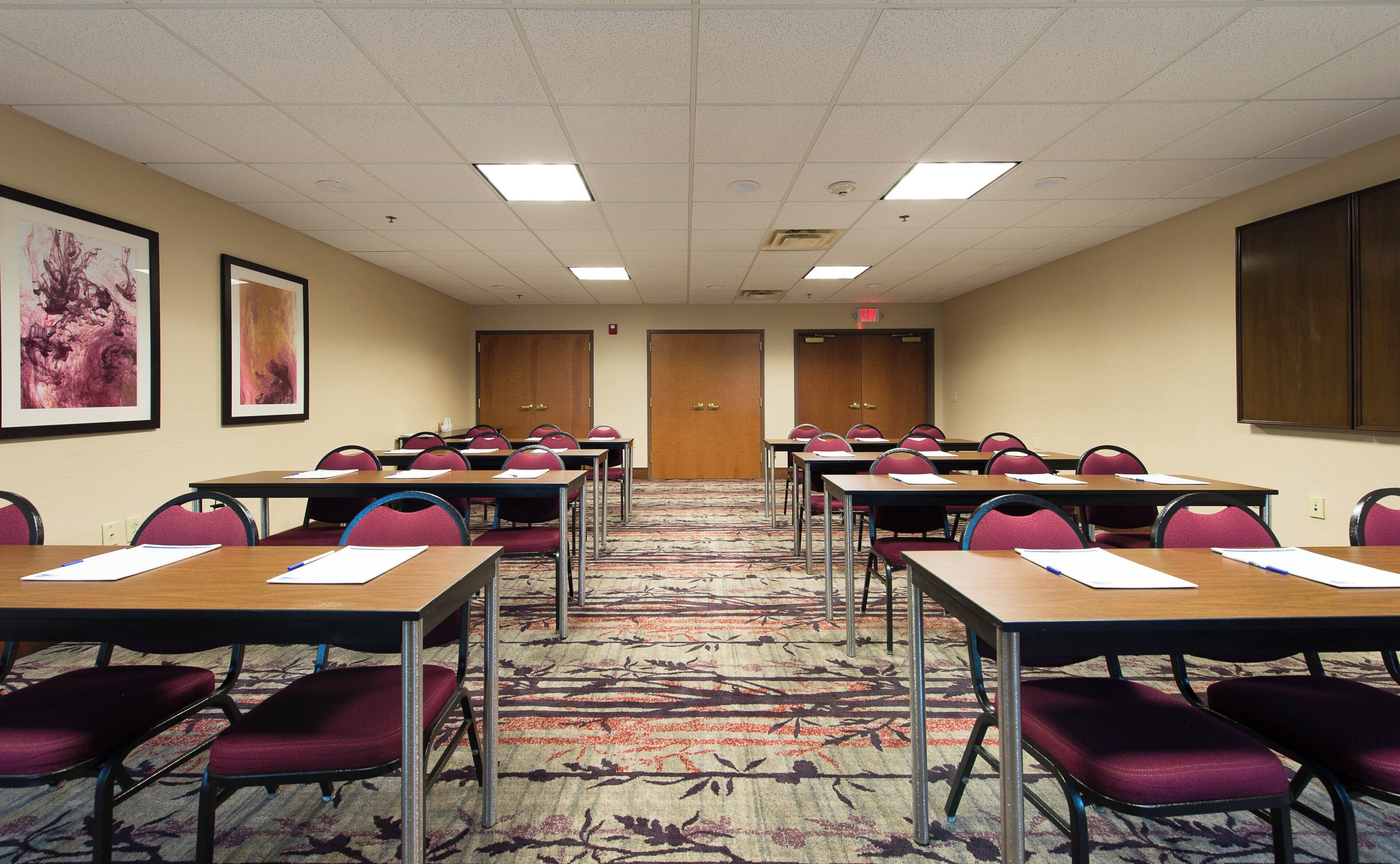 A conference room with multiple tables and chairs, a patterned carpet, and framed artwork on the walls.