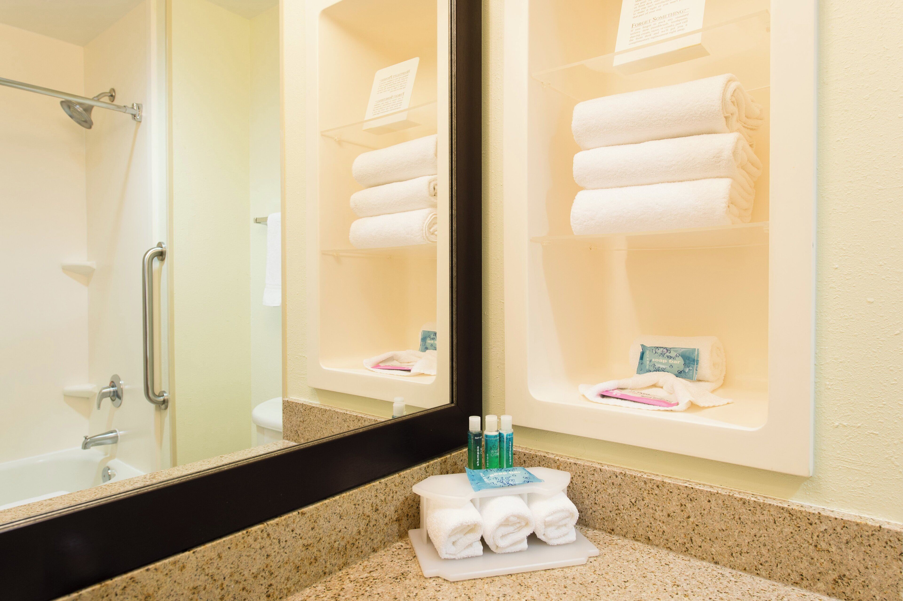 A bathroom with a shower, a sink with a mirror, and a towel rack with folded towels.