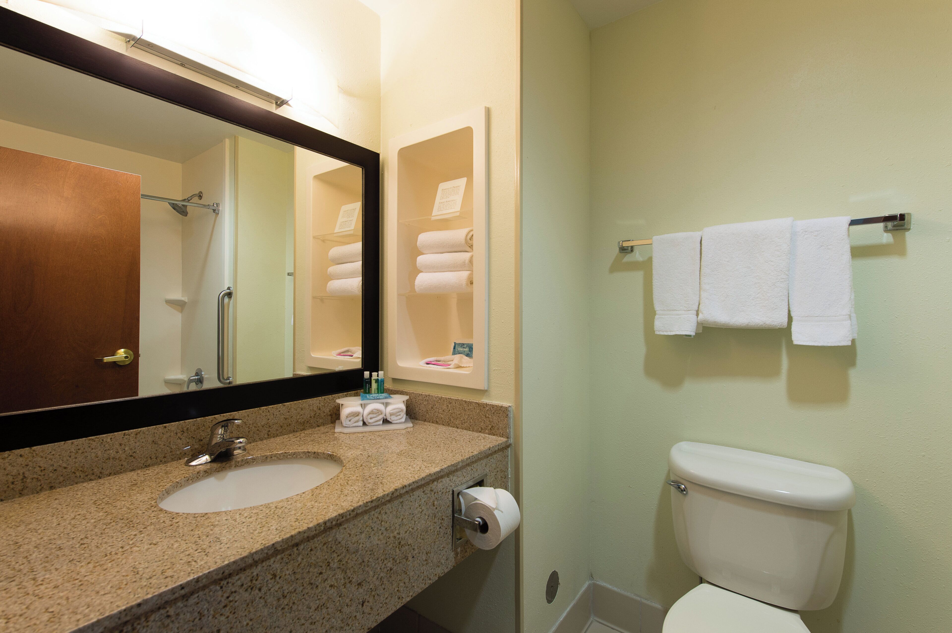 Un baño con lavamanos, espejo, toallero y retrete.