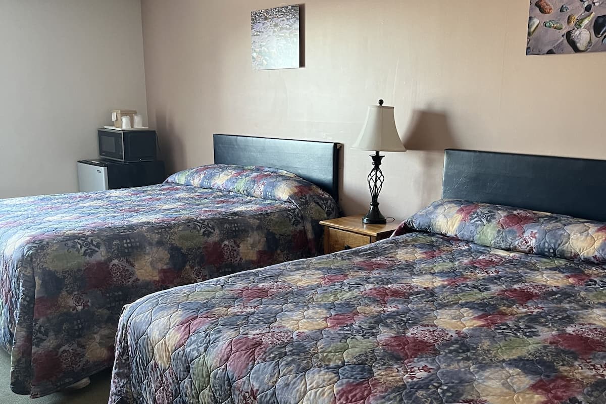 Quarto de hotel com duas camas, uma mesa de cabeceira, uma luminária e um micro-ondas.