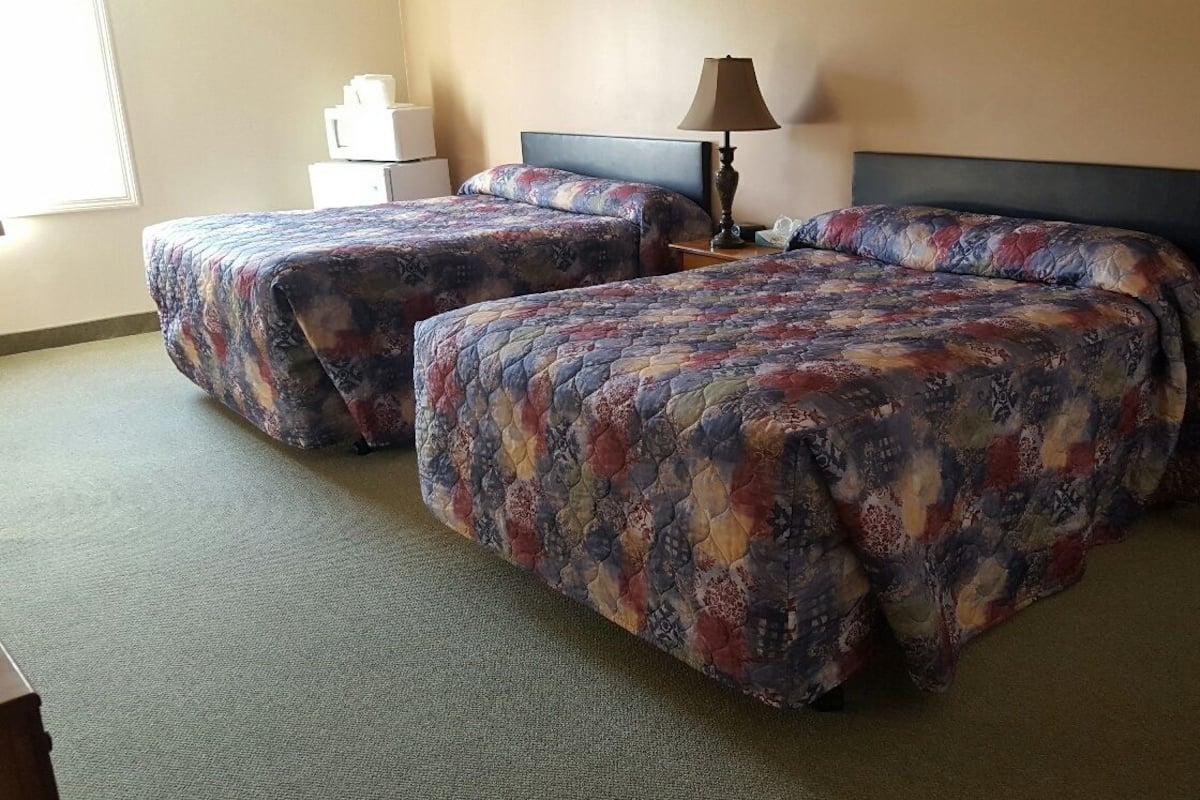 Quarto de hotel com duas camas, uma luminária e uma mesa pequena com telefone.