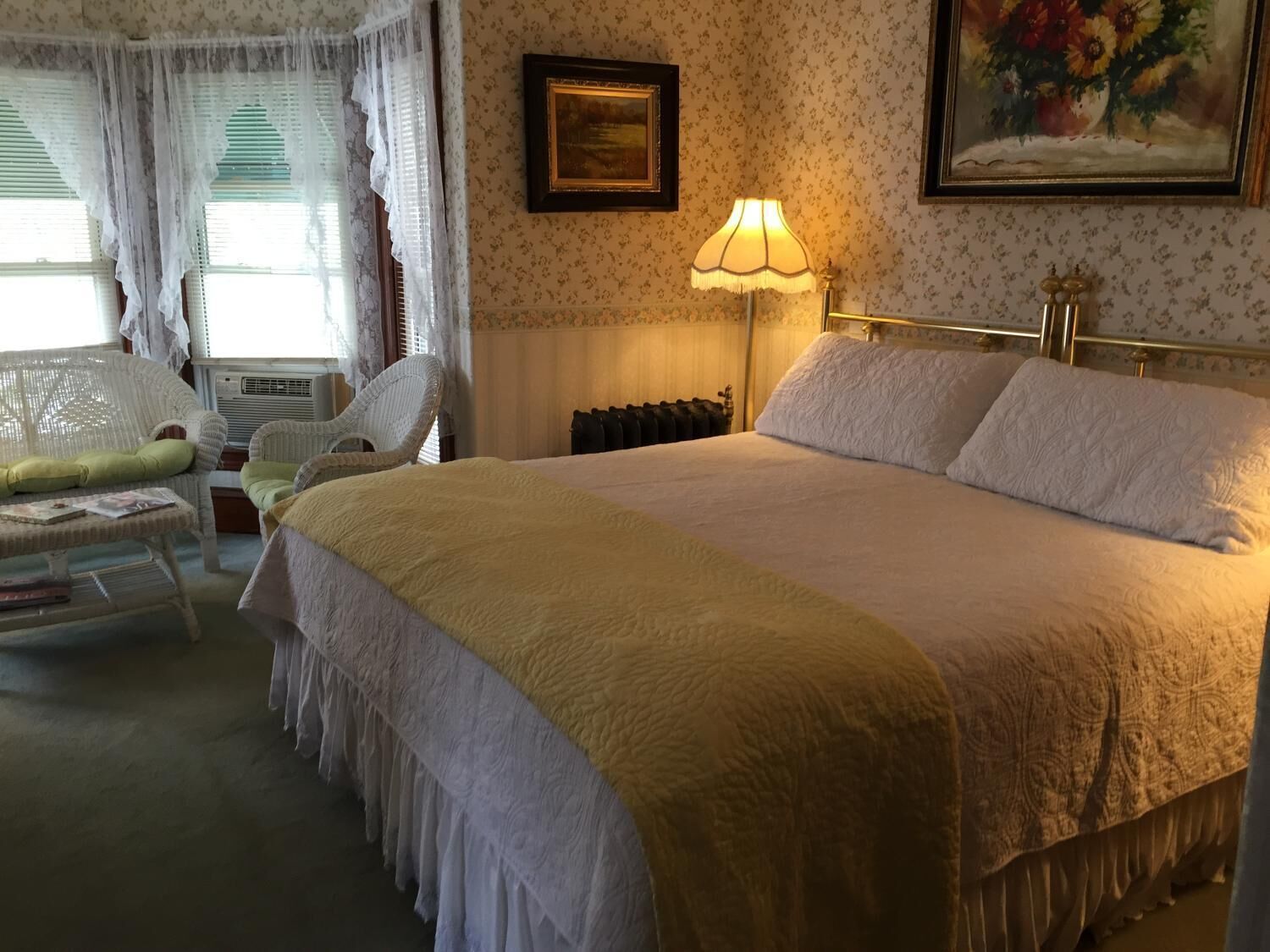 Une chambre avec un grand lit, une lampe de chevet, un radiateur et une chaise avec un coussin.