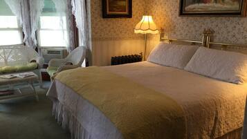 Une chambre avec un grand lit, une lampe de chevet, un radiateur et une chaise avec un coussin.