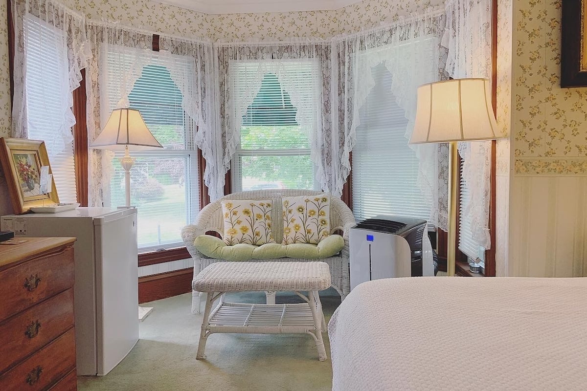 Un dormitorio con cama, una silla, un aparador y un radiador.