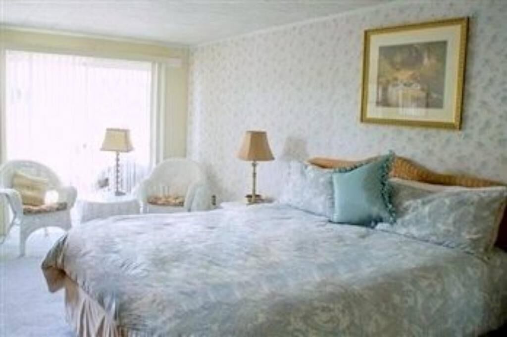 A bedroom with a large bed, two bedside tables, a chair, and a window with curtains.