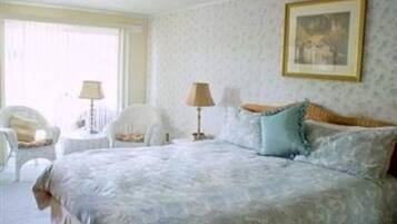 A bedroom with a large bed, two bedside tables, a chair, and a window with curtains.