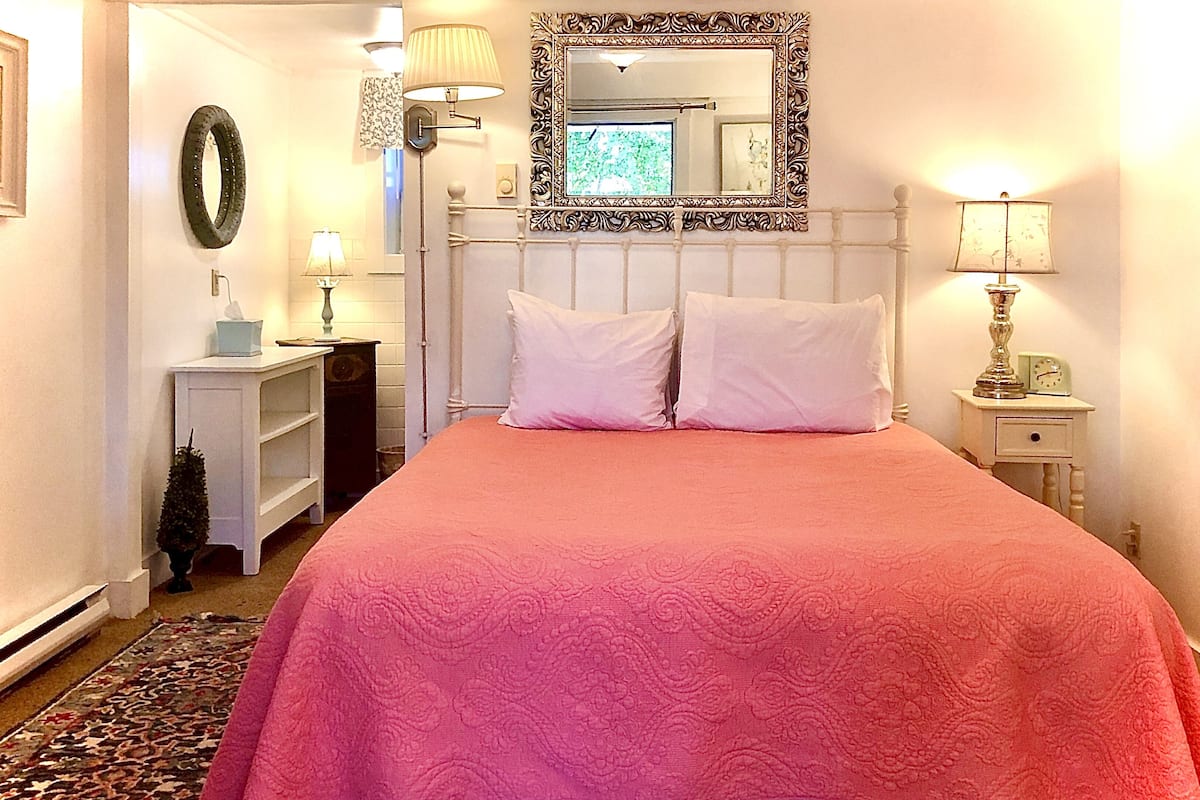 Un dormitorio con una cama grande, una mesita de noche, un espejo y una lámpara de pared.