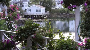 Une maison au bord du lac, avec une jetée qui s’avance sur l’eau, entourée d’une végétation luxuriante et de plantes en fleurs.
