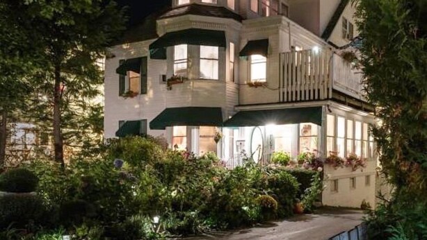 Une grande maison à deux étages, dotée d’une tourelle imposante et de nombreuses fenêtres, et entourée d’une végétation luxuriante.