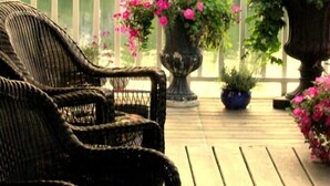 Une terrasse en bois avec des chaises en osier et des paniers de fleurs suspendus.