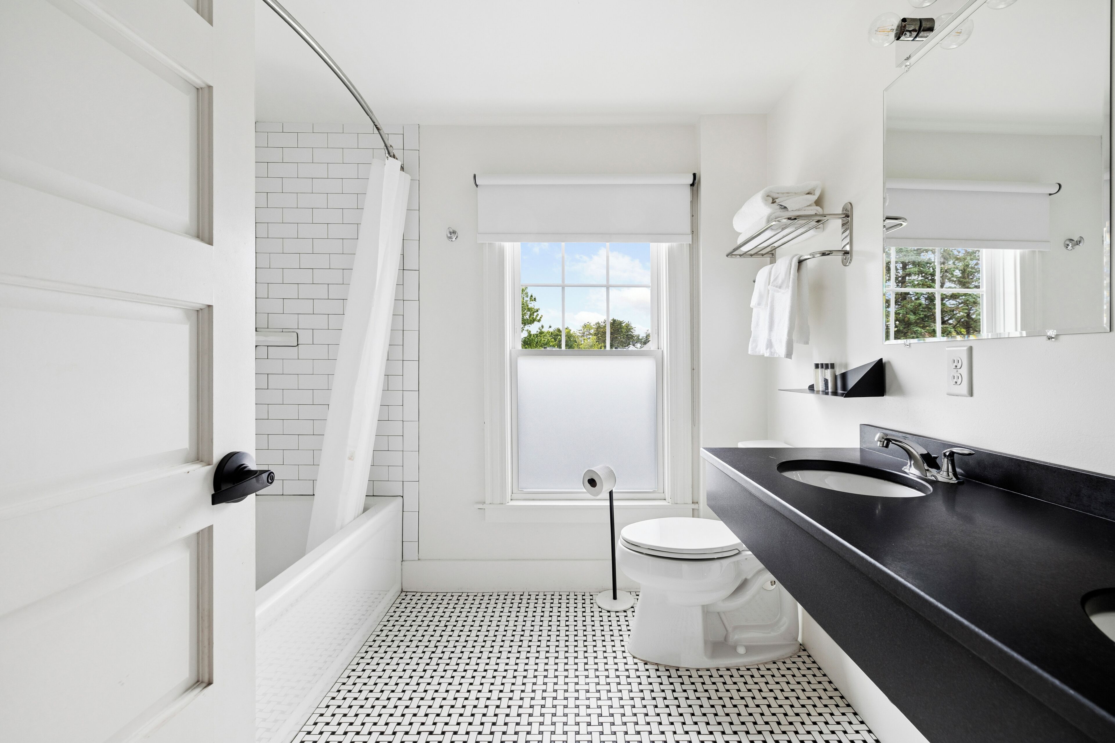 A modern bathroom with a black countertop, white fixtures, and a view of greenery outside.