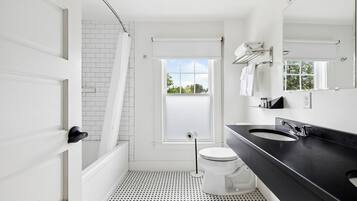 A modern bathroom with a black countertop, white fixtures, and a view of greenery outside.