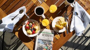 Una mesa de madera con alimentos para el desayuno, un periódico y una taza de café.