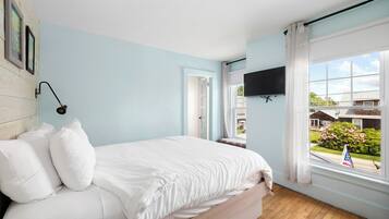 A bedroom with a bed, a mounted TV, a window with curtains, and a view of the outside.