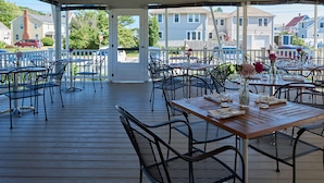 An outdoor patio with tables and chairs, a wooden deck, and a view of residential buildings. - Higgins Beach Inn (Scarborough)