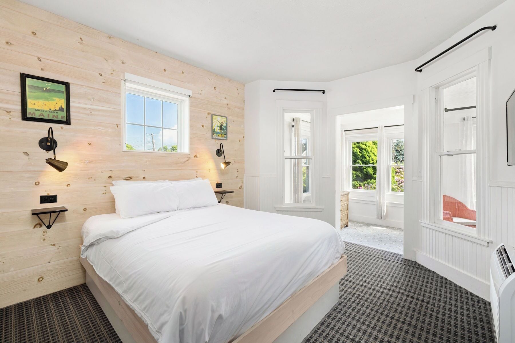 A bedroom with a bed, two bedside lamps, a window, and a door leading to an outdoor area.