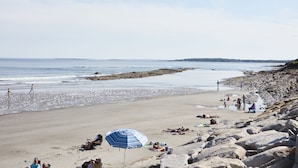 A beach with people relaxing, a blue umbrella, and rocky terrain. - Higgins Beach Inn (Scarborough)