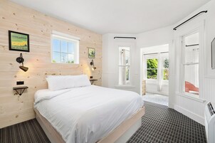 Un dormitorio con cama, dos lámparas de pared, una ventana y una puerta que da a un área exterior.