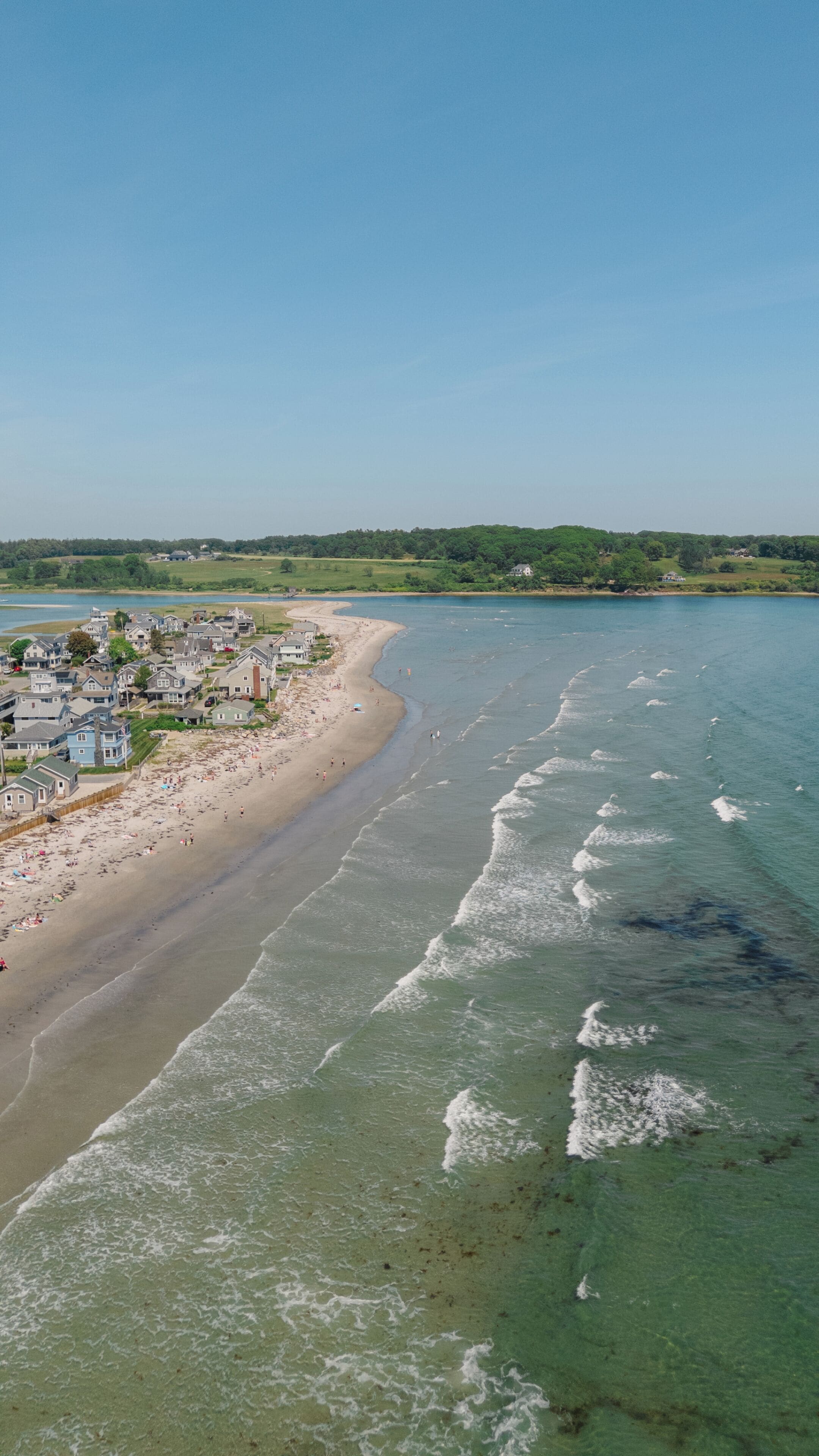 Una spiaggia costiera con acque limpide, una riva sabbiosa e una zona residenziale con case e un ombrellone.