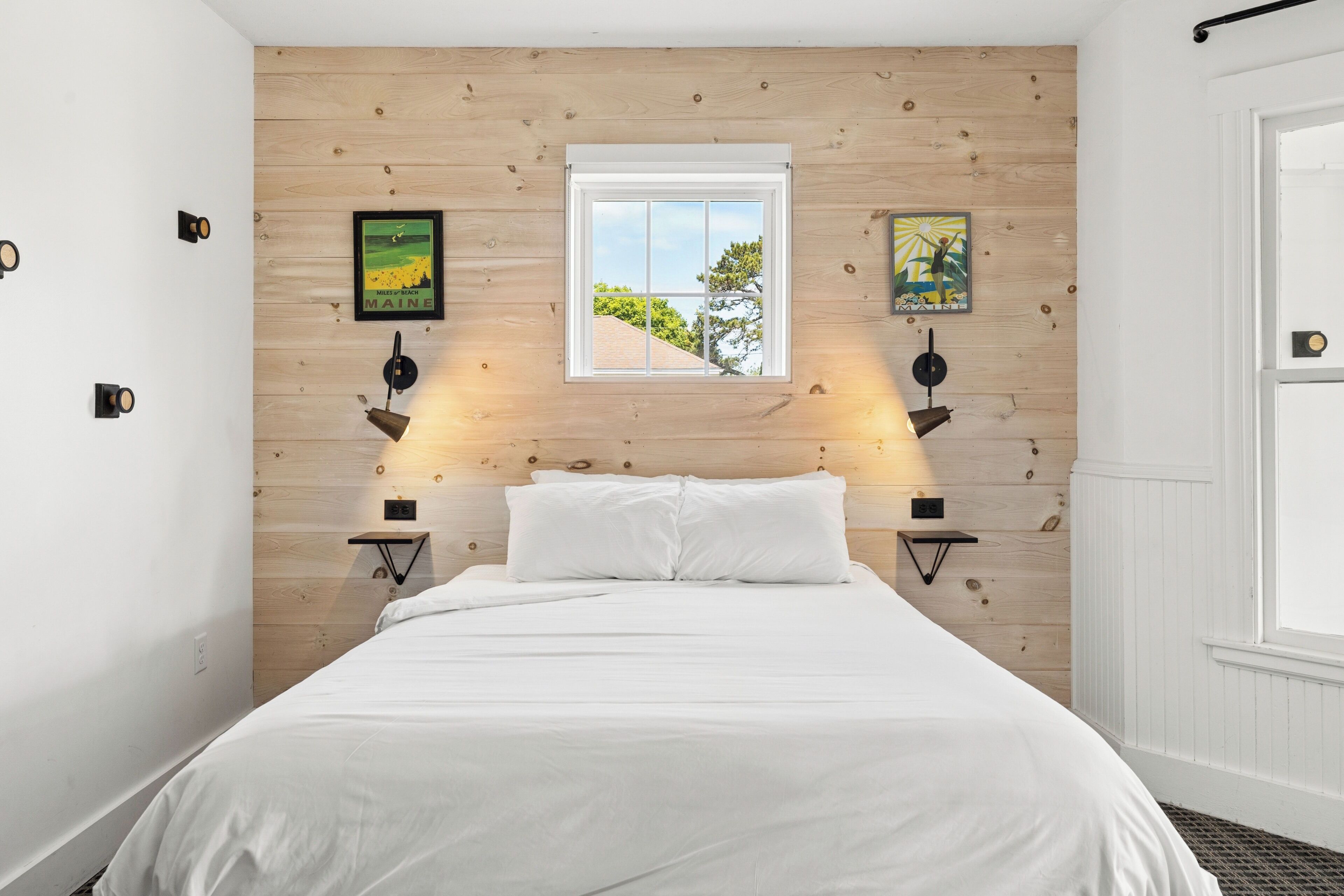 A bedroom with a wooden headboard, a bed with white bedding, two wall-mounted lamps, and two framed pictures.