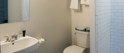 A bathroom with a white sink, toilet, and a shower area with tiled walls.