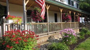 A two-story house with a porch, a hanging American flag, and flower planters. - Inn By The River (West Forks)
