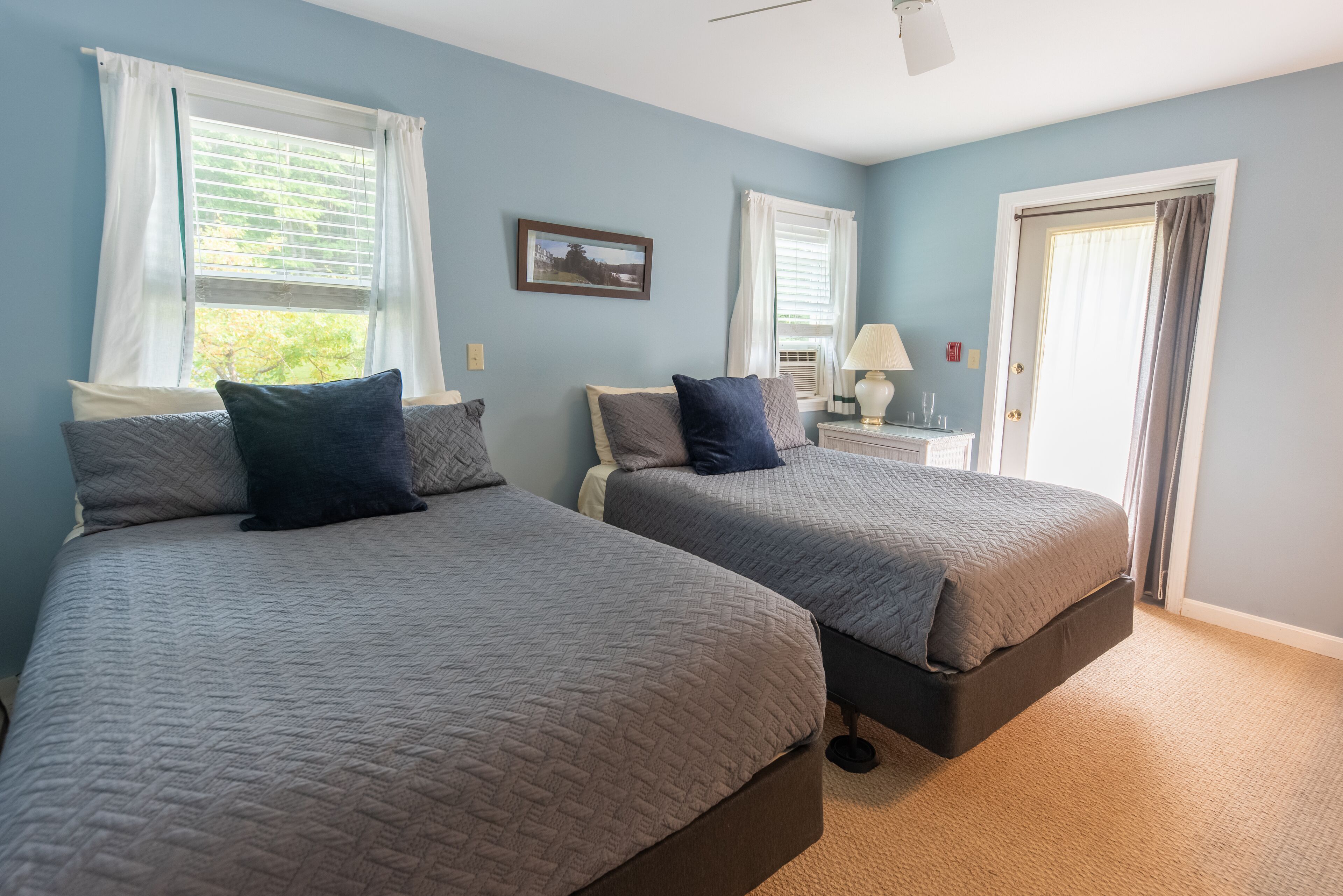 A bedroom with two beds, a nightstand, a lamp, and a door.