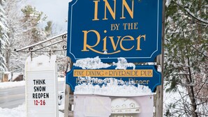 A sign for 'Inn by the River' with a snow-covered signpost and a 'Think Snow Reopen 12-26' sign. - Inn By The River (West Forks)