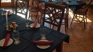 A dining area with a table set for six, wooden chairs, and a view of a lake through large windows. - Inn By The River (West Forks)