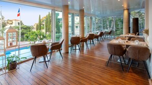 Un restaurante con piso de madera, ventanas amplias y vistas a una piscina y follaje.