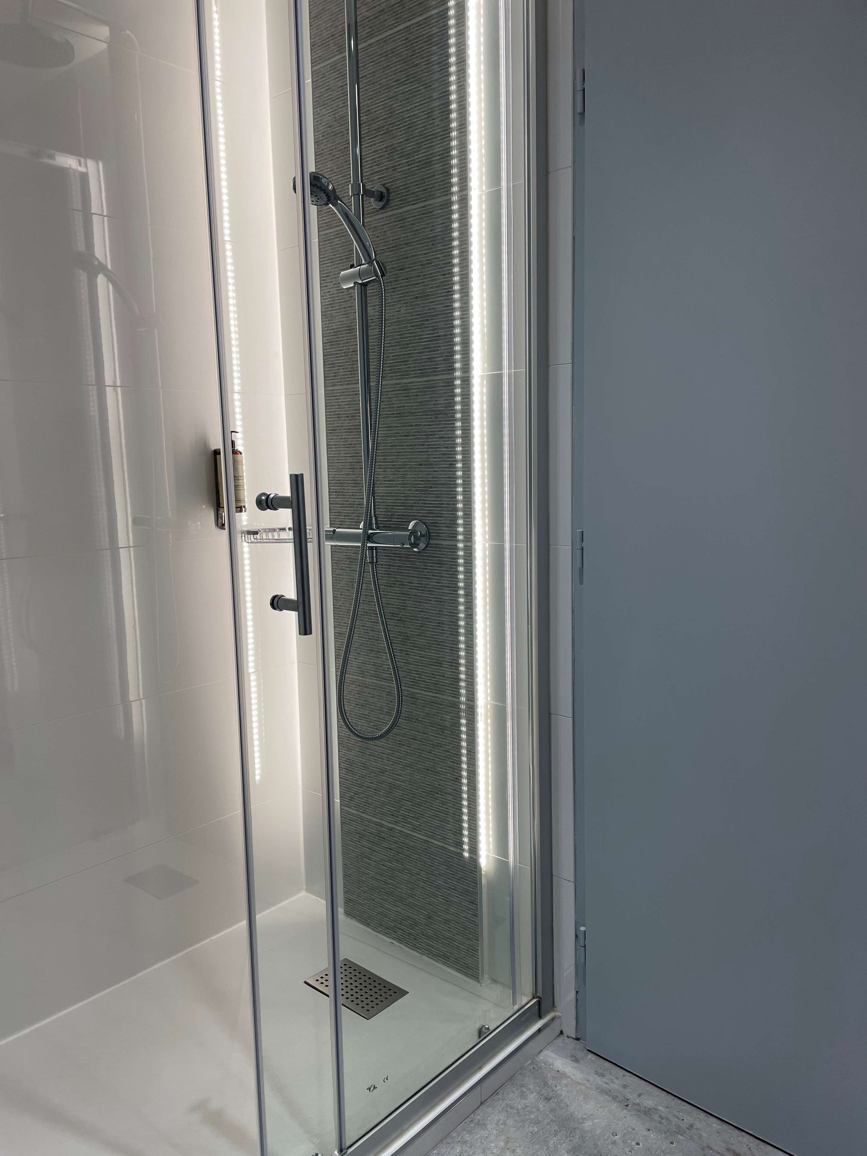 A modern shower enclosure with a glass door, a handheld showerhead, and a wall-mounted control panel.