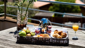 Desayuno con frutas, pasteles y bebidas sobre una mesa, con una vista panorámica al mar.