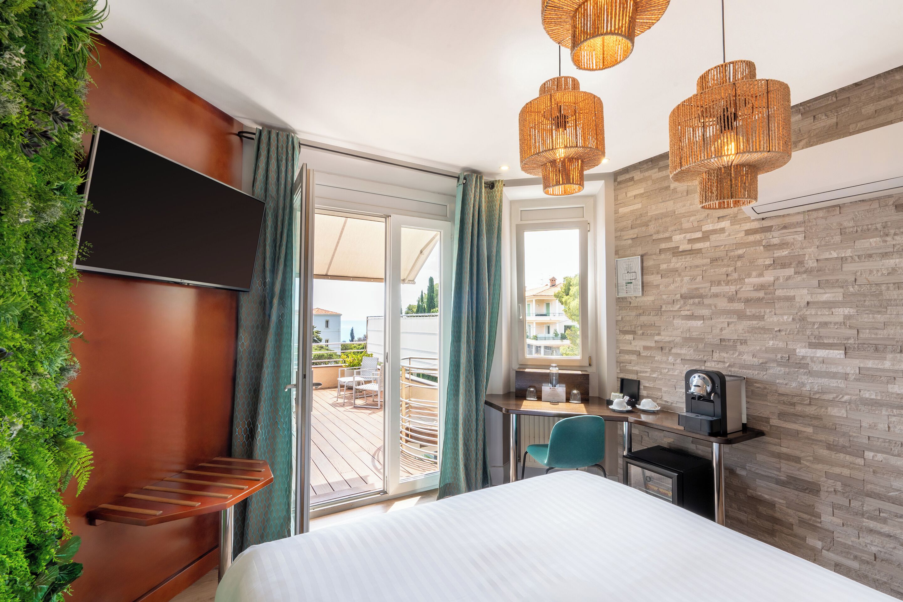 A hotel room with a bed, a desk with a coffee machine, a TV, and a balcony with a view.