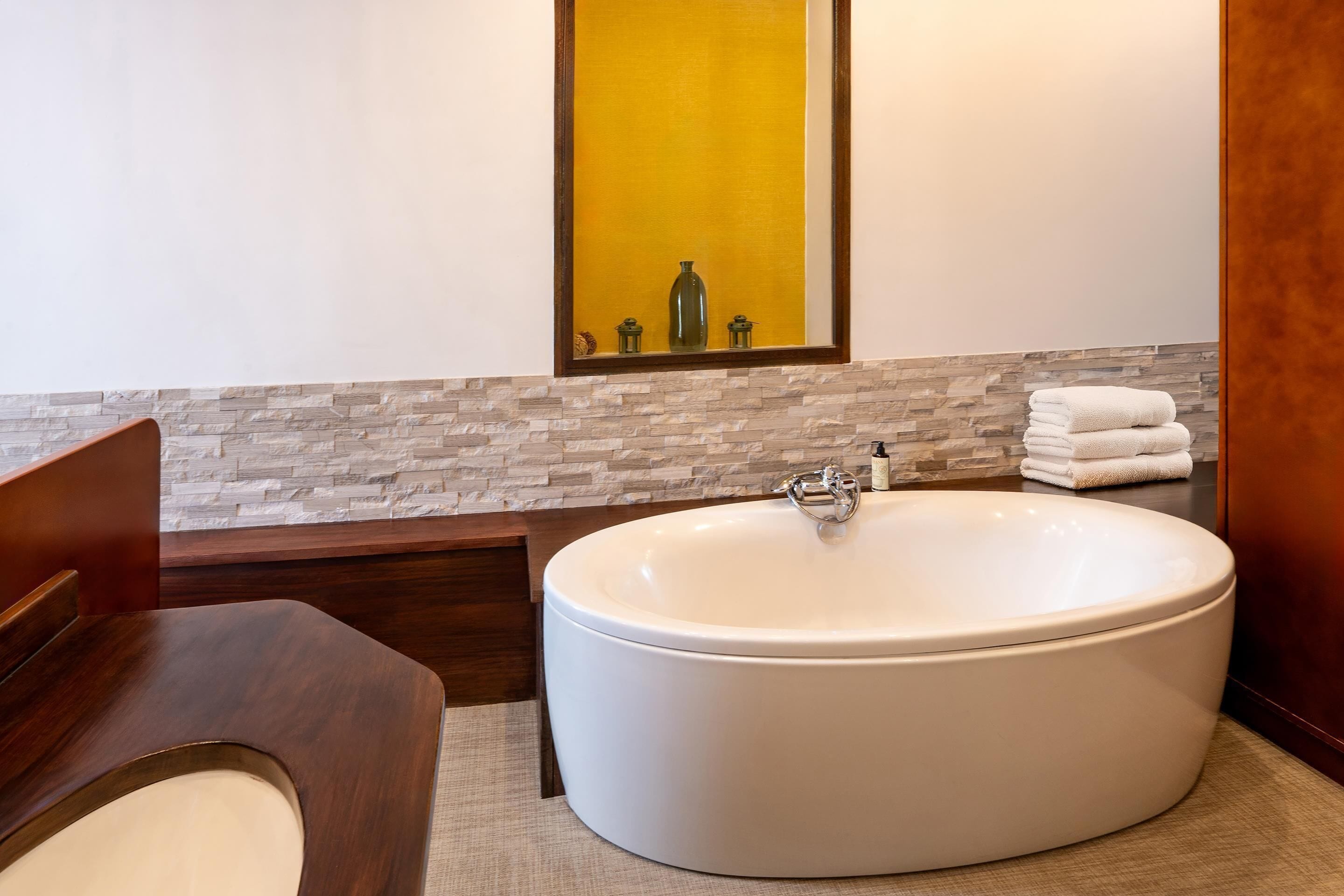Une salle de bain moderne avec une grande baignoire, un meuble-lavabo en bois et un miroir placé devant un mur jaune.