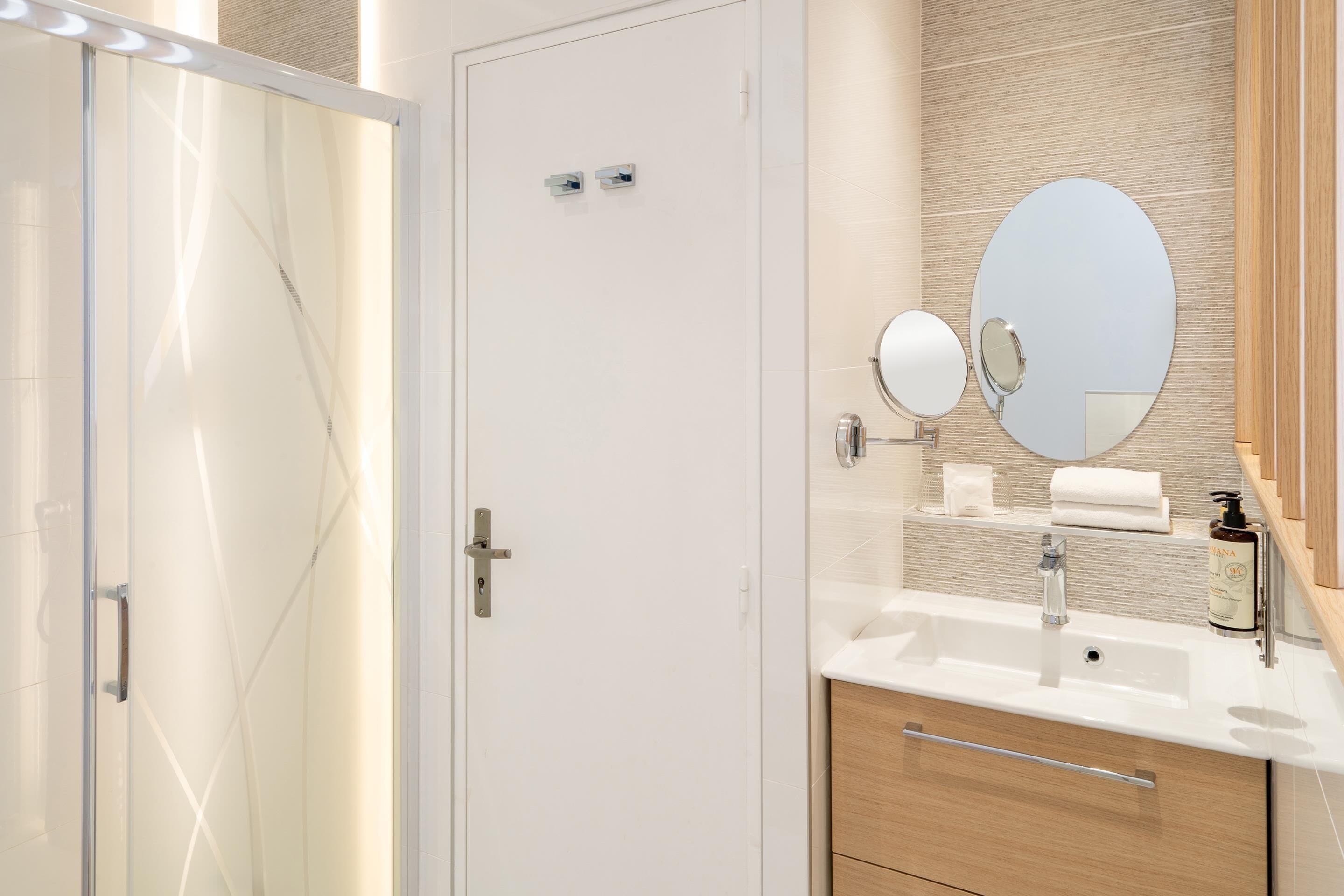 A modern bathroom with a glass shower door, a white sink with a mirror, and wooden cabinetry.