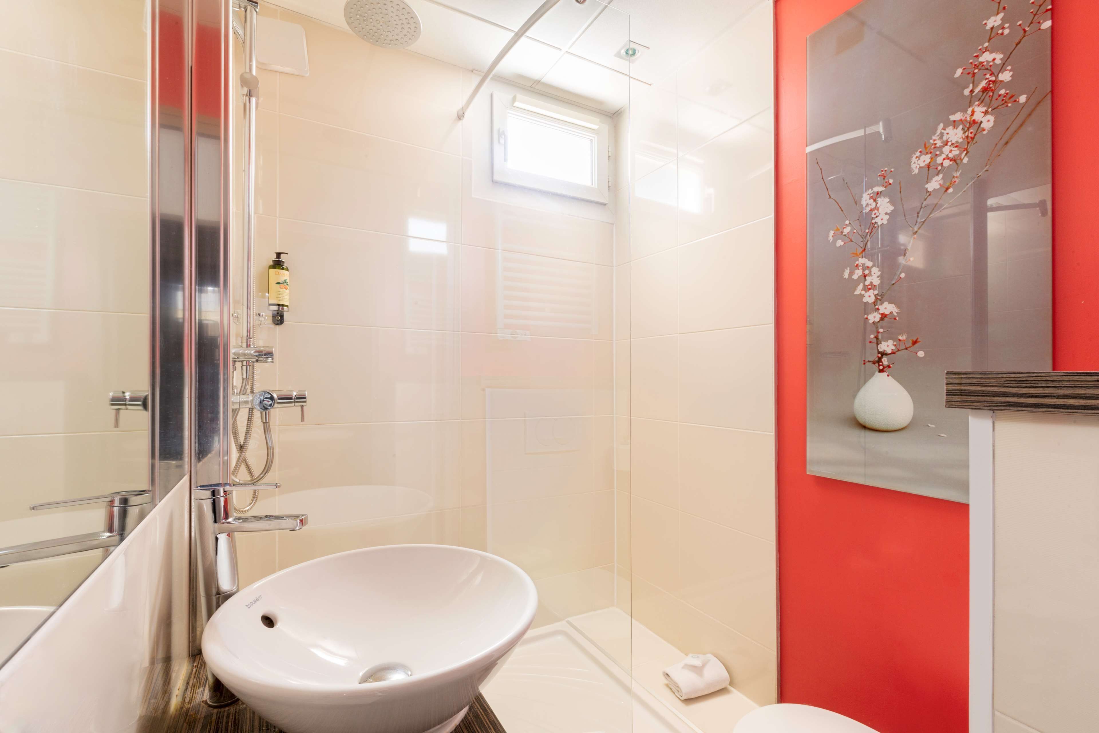 A modern bathroom with a glass shower enclosure, a white sink, and a red accent wall.