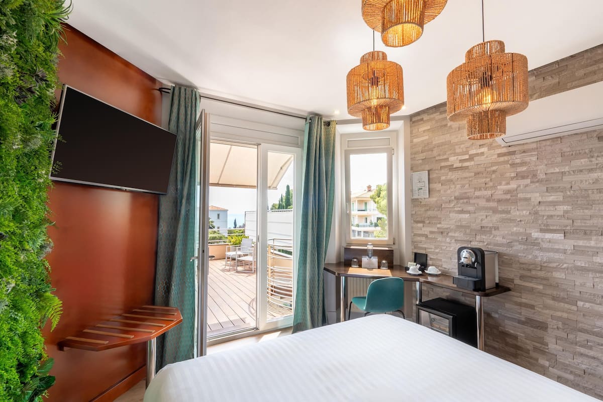 A hotel room with a bed, a desk, a chair, a television, and a view of the outdoor area.