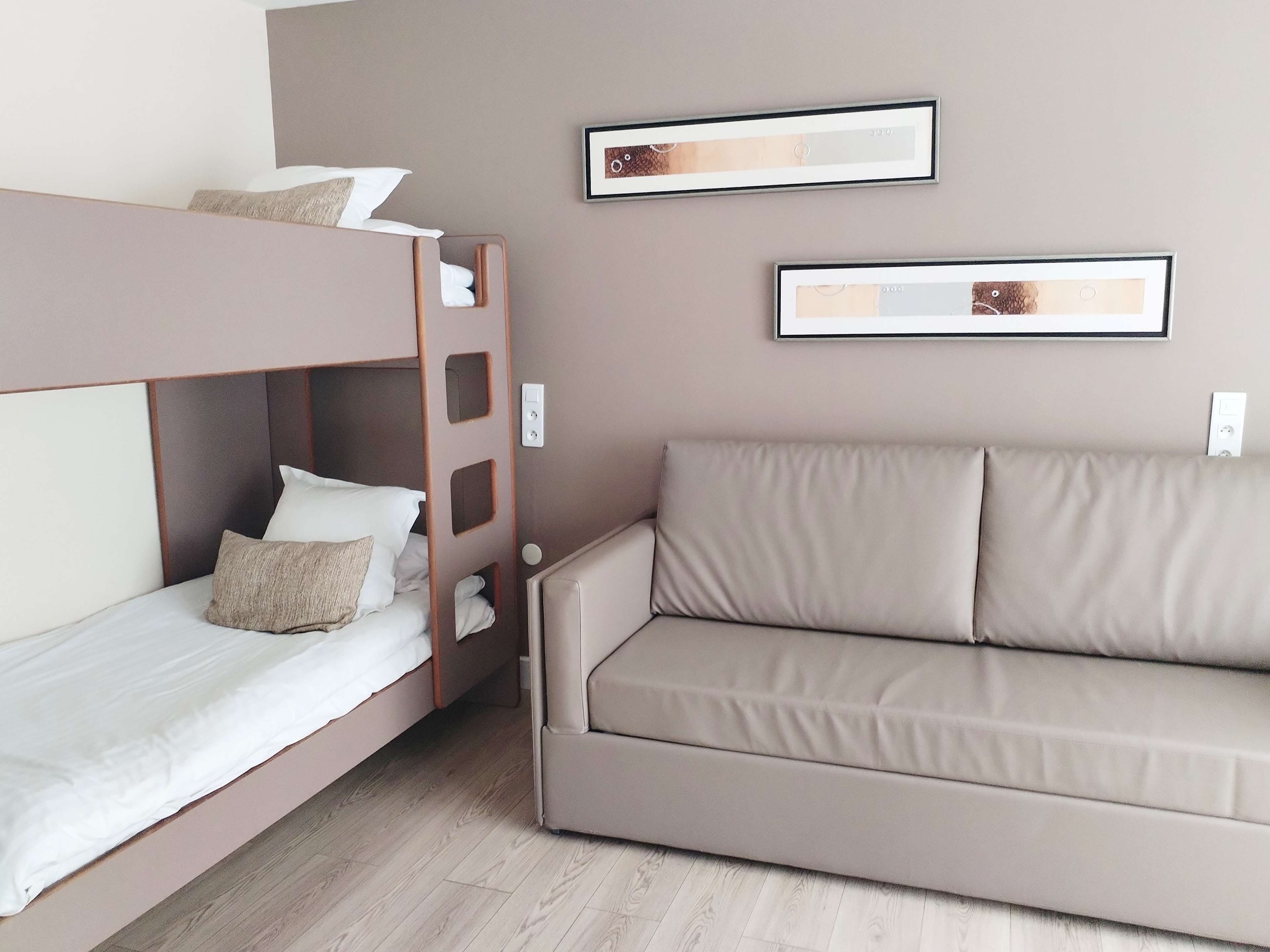 A hotel room with a bunk bed, a sofa, and two framed pictures on the wall.