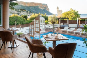 Un área junto a la piscina con sillones de descanso, una mesa preparada para comer y vistas al mar y a las montañas.