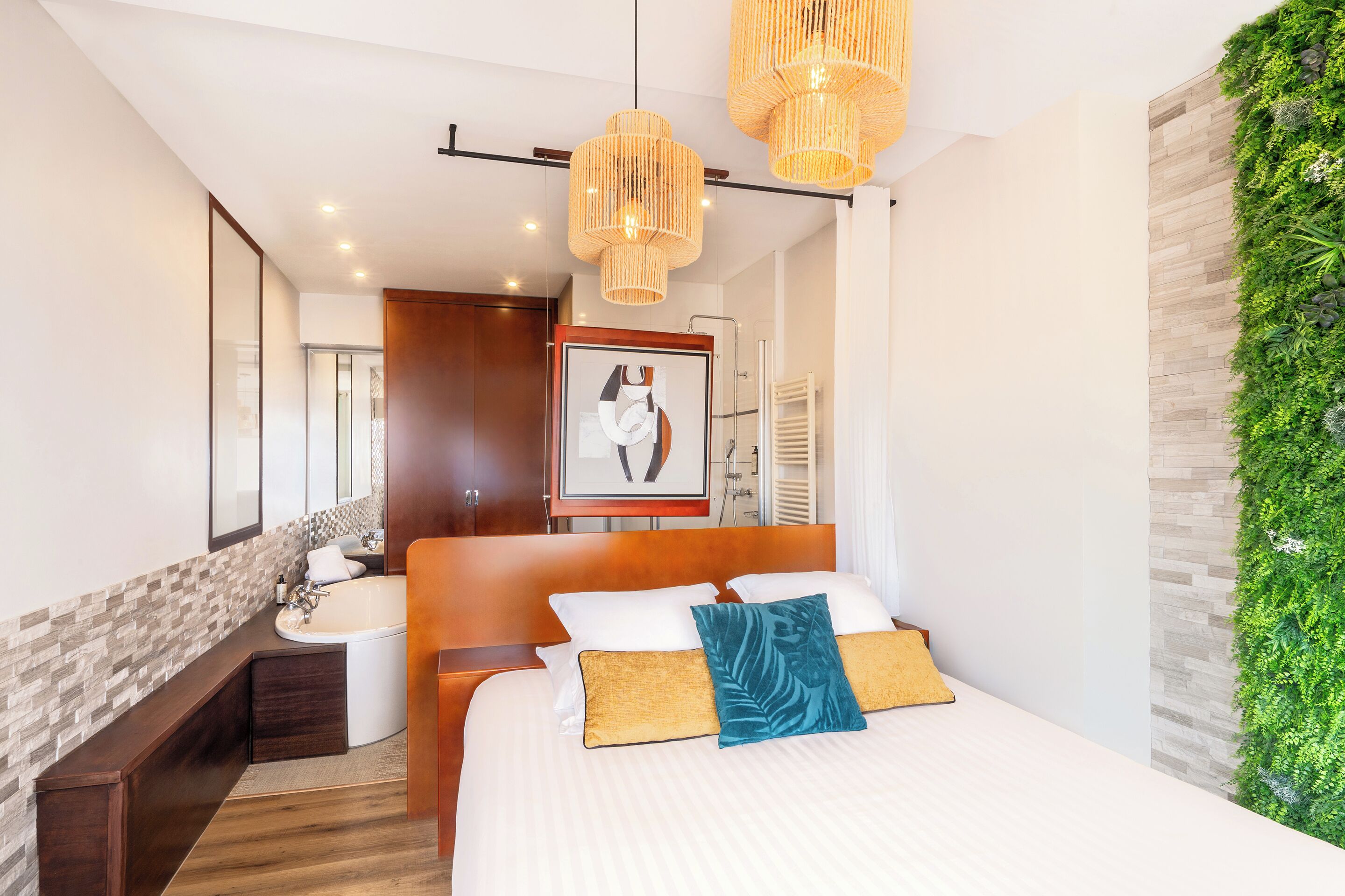 A modern hotel room with a large bed, a wooden headboard, a built-in sink, and a green vertical garden wall.