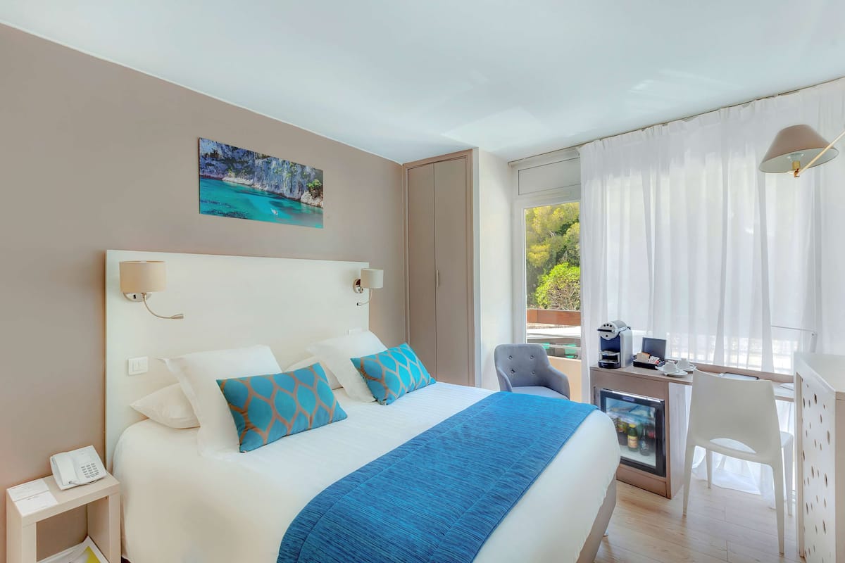 A hotel room with a bed, a desk with a computer, a chair, a phone, and a small fridge.