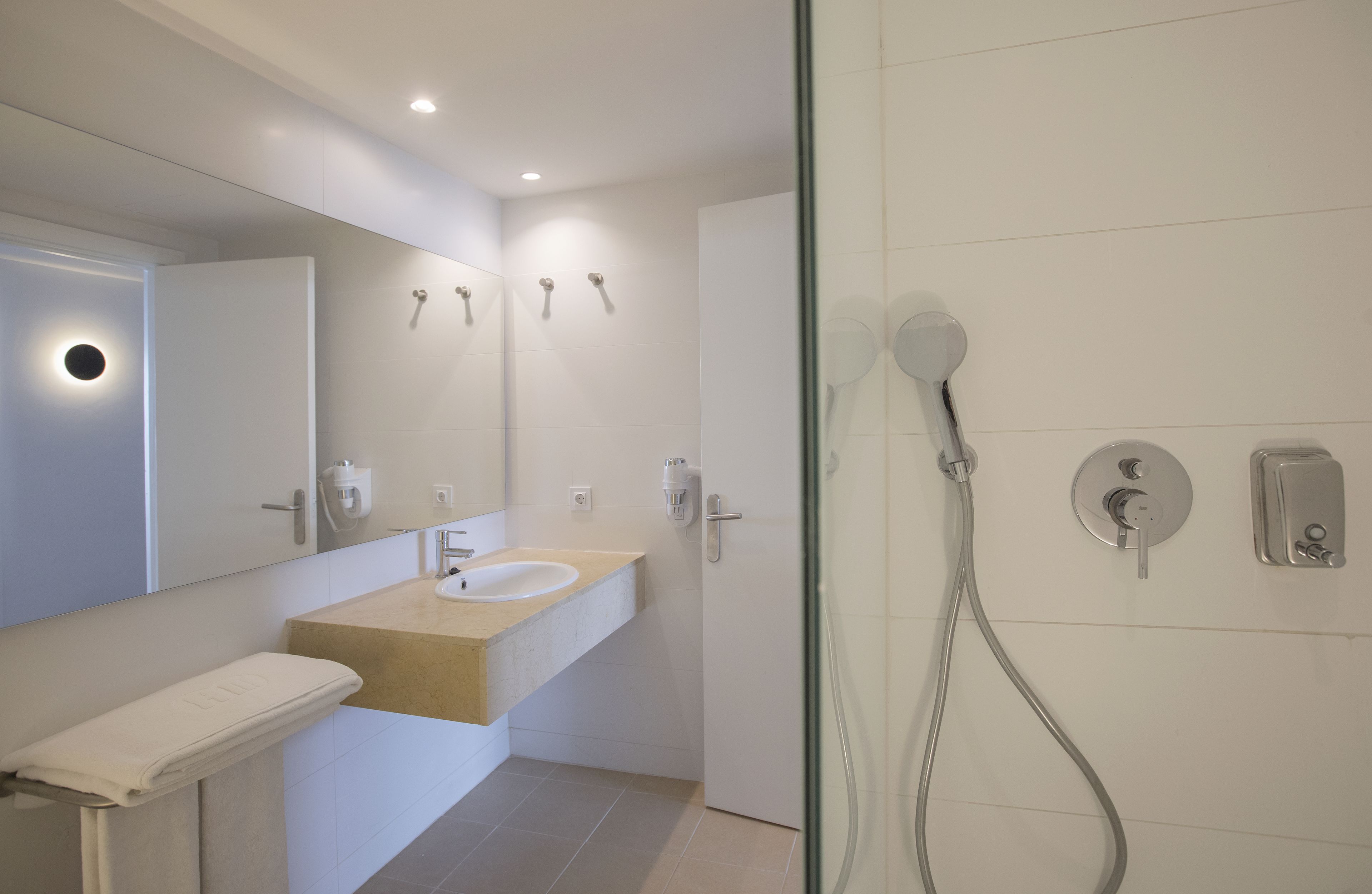 Un baño moderno con cabina de ducha de vidrio, un lavamanos con encimera color beige y un espejo sobre el lavamanos.