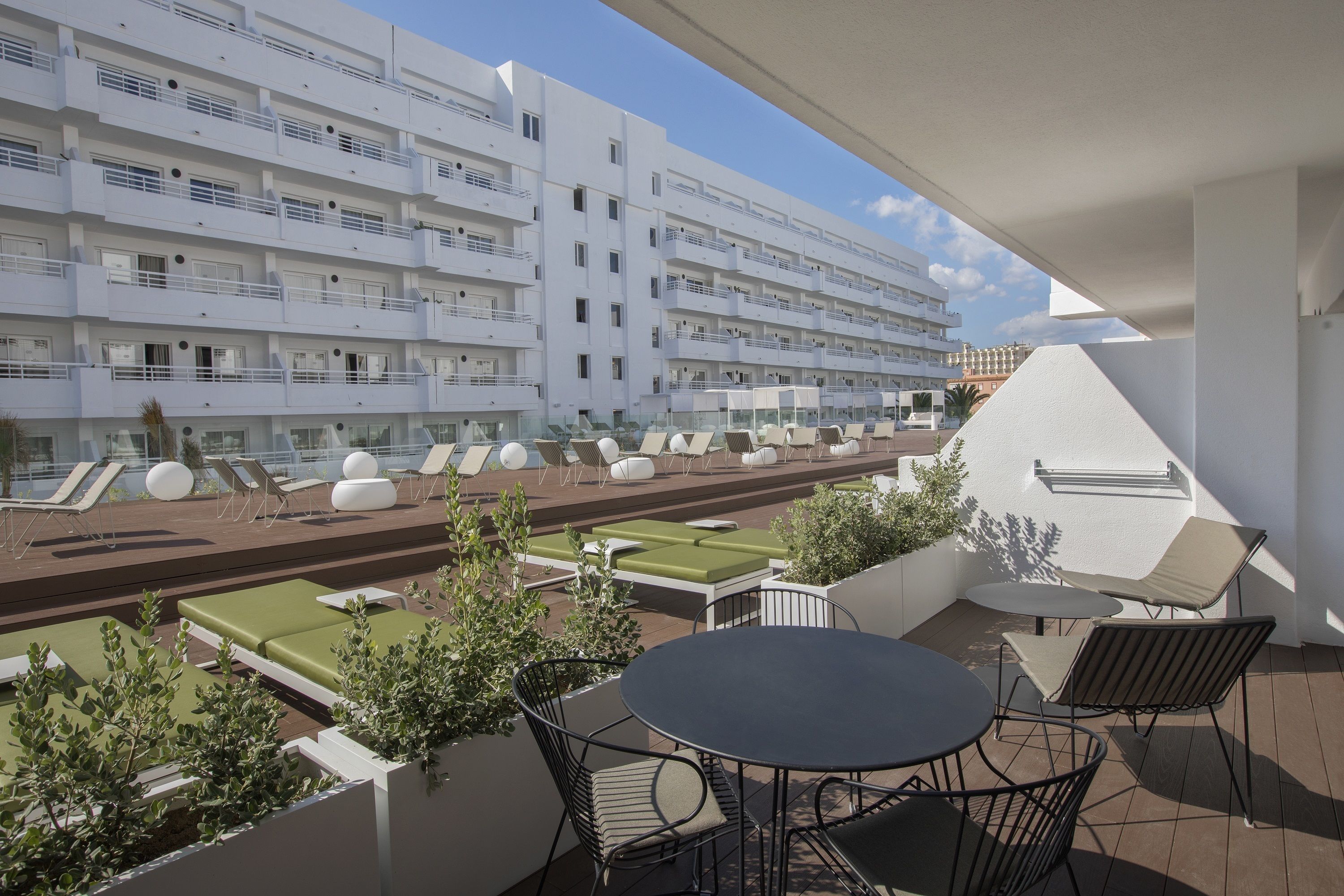 Une terrasse sur le toit avec des sièges extérieurs, une piscine et une vue sur un immeuble blanc doté de balcons.