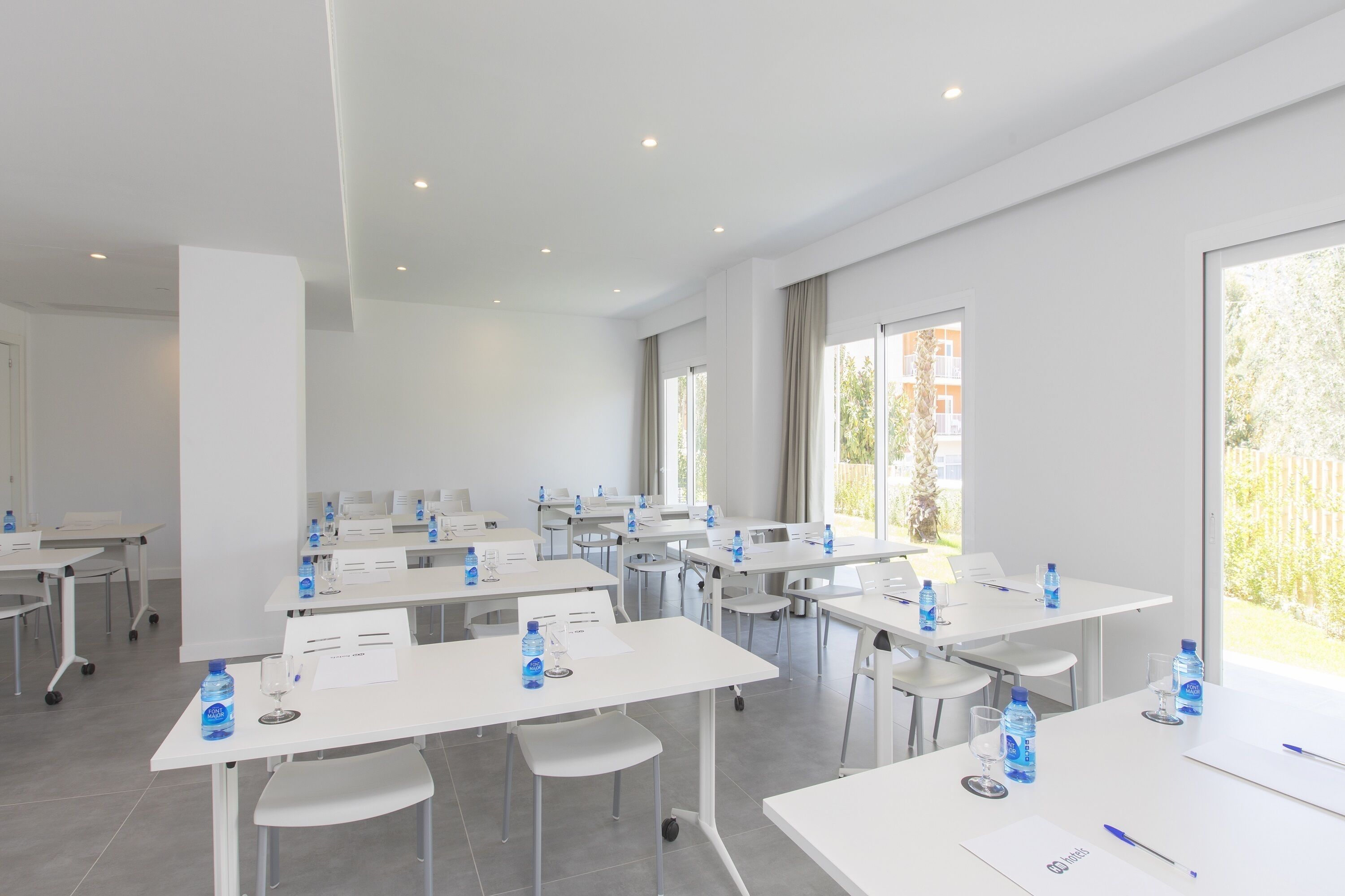 Un salón de conferencias con mesas blancas, sillas y botellas de agua.