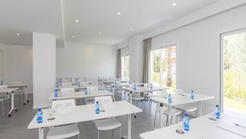 Un salón de conferencias con mesas blancas, sillas y botellas de agua.