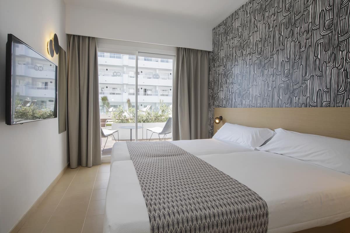 A hotel room with a large bed, a patterned wall, a view of the outside balcony, and a framed picture on the wall.