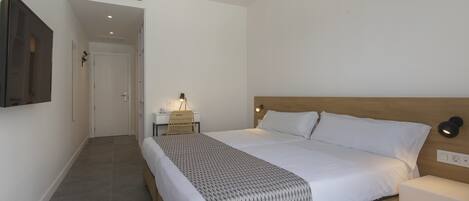 Een slaapkamer met een houten bed, witte beddengoed, een bedlampje en een aan de muur bevestigde televisie.