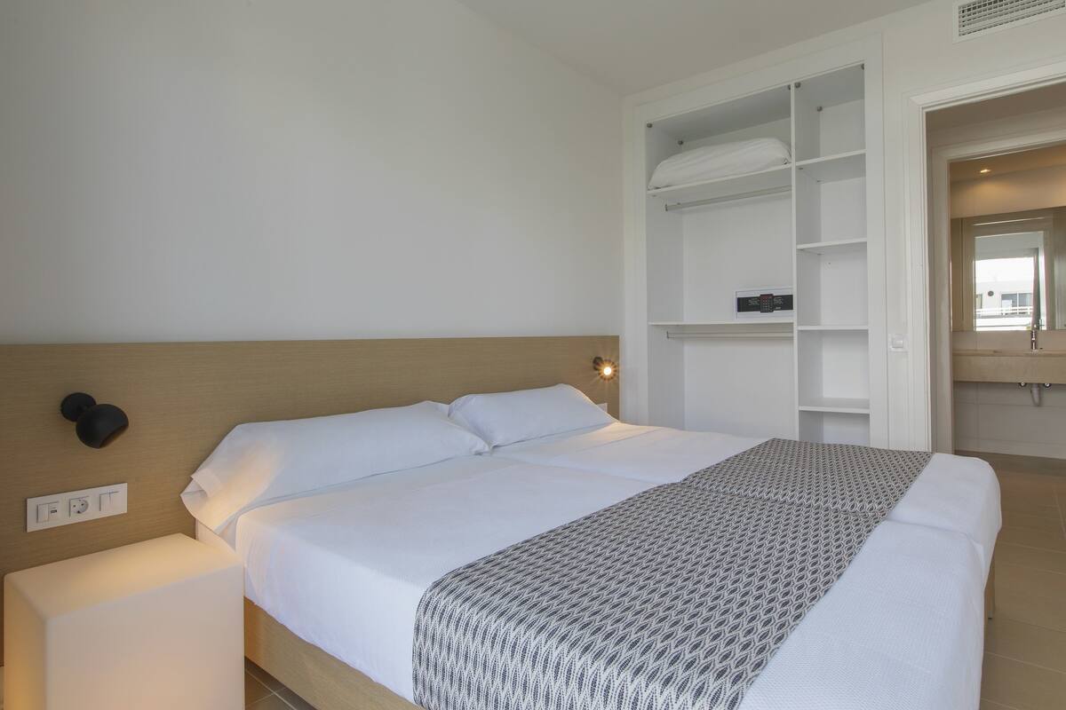 A neatly made bed with a patterned throw, a bedside lamp, and a built-in shelving unit above the bed.
