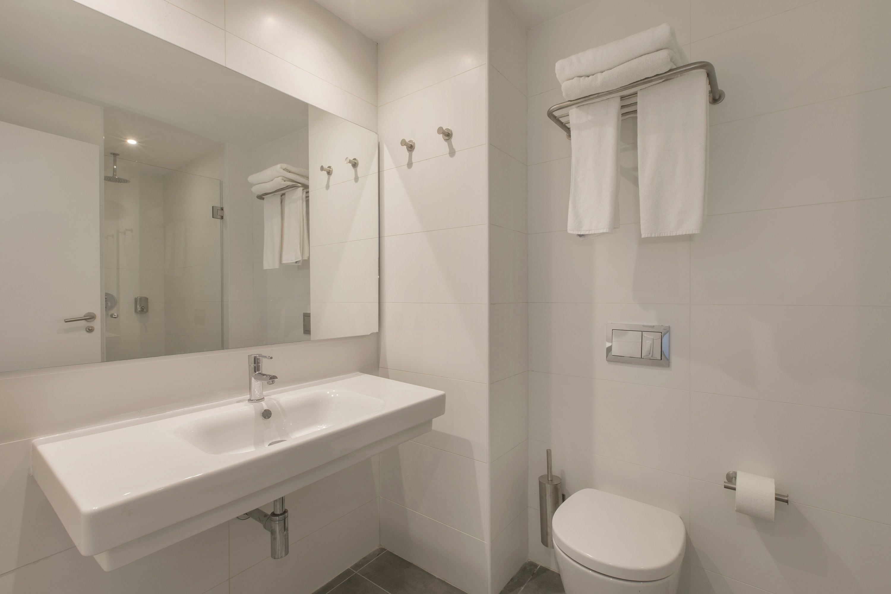 Un baño moderno con un lavabo blanco, un inodoro, una ducha y un perchero para toallas.